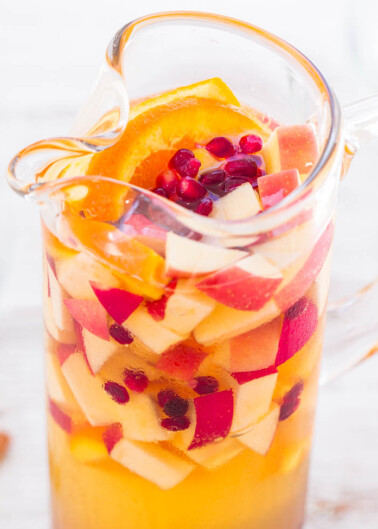 A pitcher filled with fruit-infused water, containing slices of oranges, apples, and pomegranate seeds.