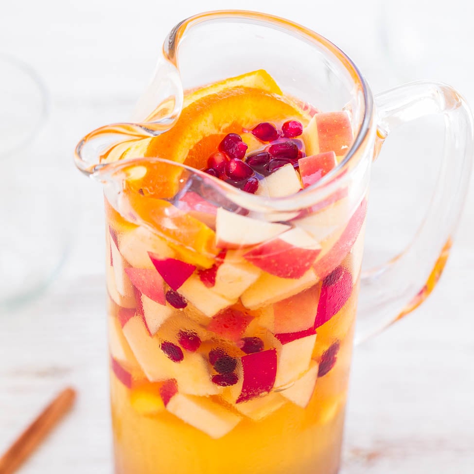 A pitcher filled with fruit-infused water, containing slices of oranges, apples, and pomegranate seeds.