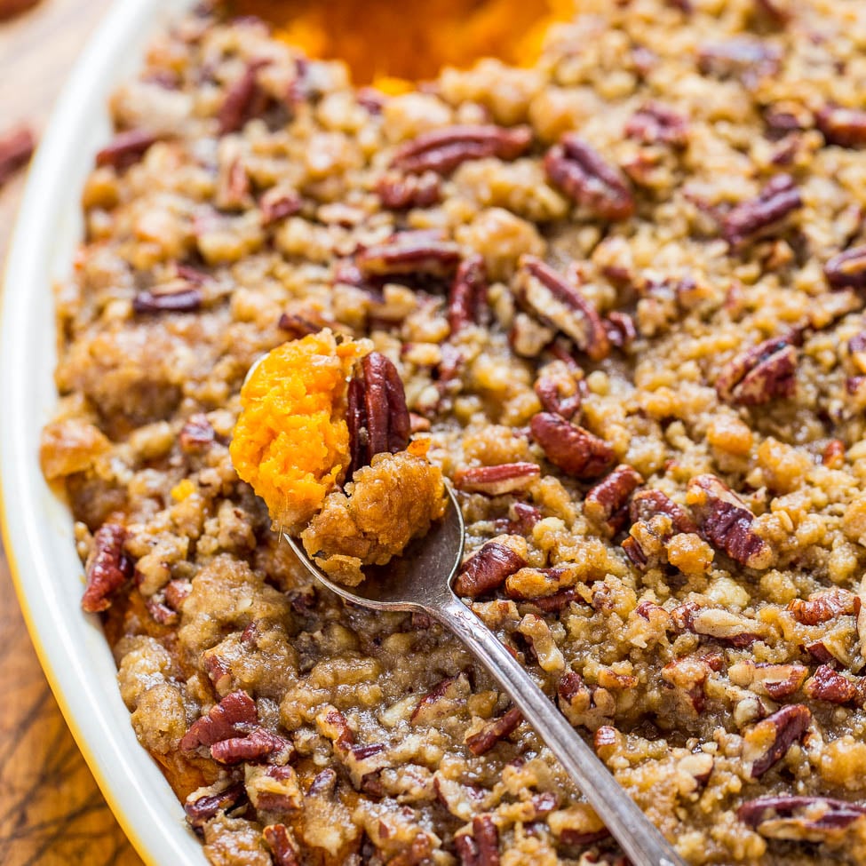 A close-up view of a sweet potato casserole topped with pecans and a serving spoon taking a portion.