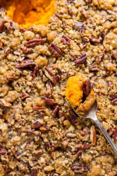 A close-up of a sweet potato casserole topped with pecans and a spoonful being lifted out.