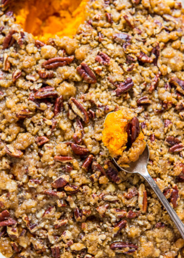 A close-up of a sweet potato casserole topped with pecans and a spoonful being lifted out.
