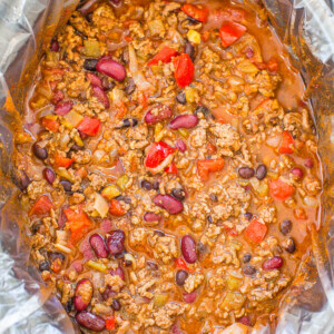 A pot of beef chili with beans and vegetables, cooking in a slow cooker lined with a disposable bag.