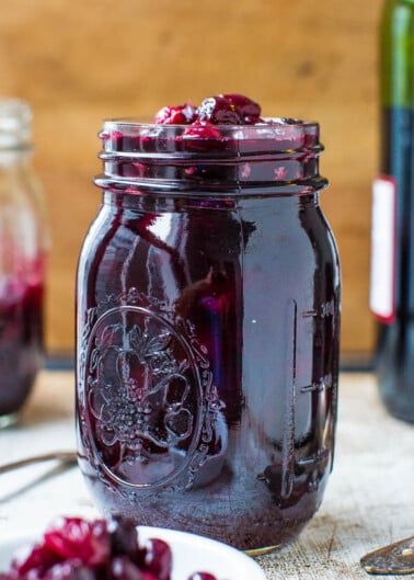 Jar of homemade berry jam on a wooden table with a wine bottle in the background.