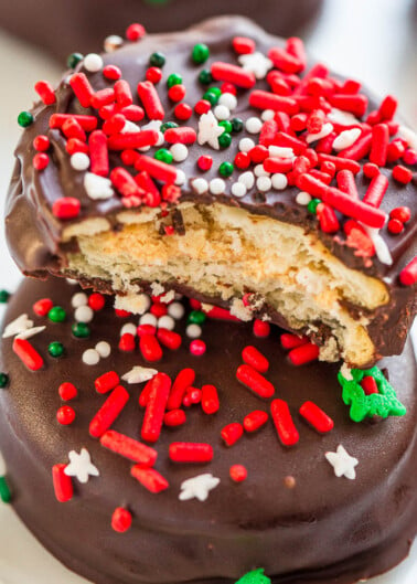 Chocolate-covered cookie with a bite taken out, topped with red and white sprinkles.
