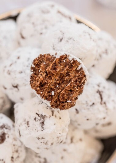 A bowl of powdered sugar-coated chocolate cookies with one cookie being held up to show the inside texture.
