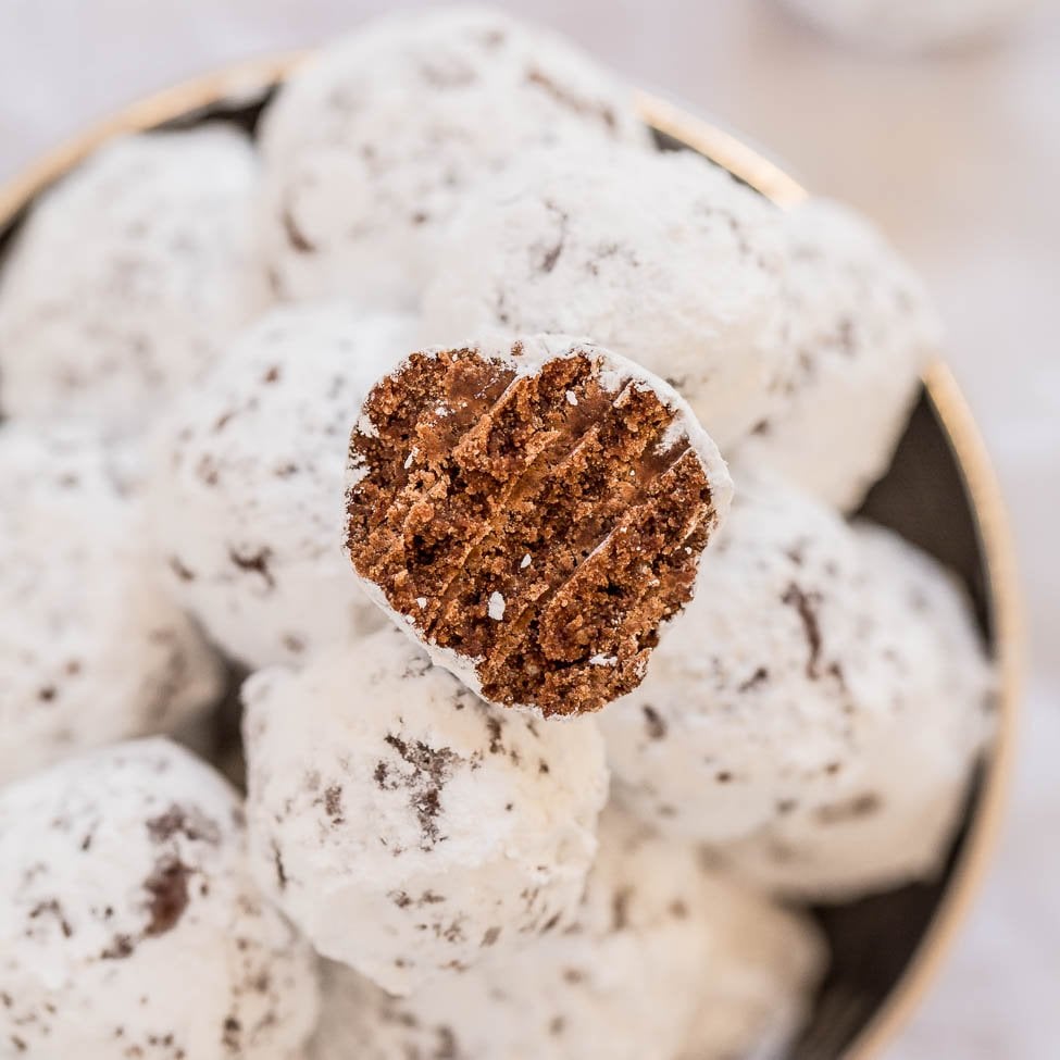 A bowl of powdered sugar-coated chocolate cookies with one cookie being held up to show the inside texture.