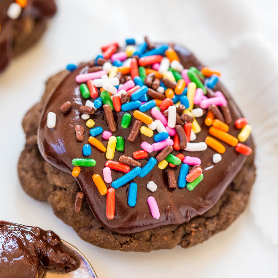A chocolate cookie topped with chocolate icing and colorful sprinkles.