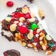 A piece of festive chocolate bark decorated with candies and sprinkles on a white surface.
