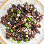 Korean beef bulgogi served over rice, garnished with green onions and sesame seeds.