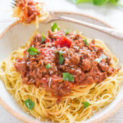 A plate of spaghetti topped with meat sauce and sprinkled with herbs and grated cheese.