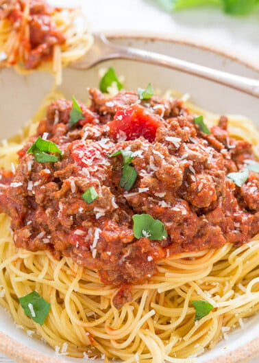 A plate of spaghetti topped with meat sauce and sprinkled with herbs and grated cheese.