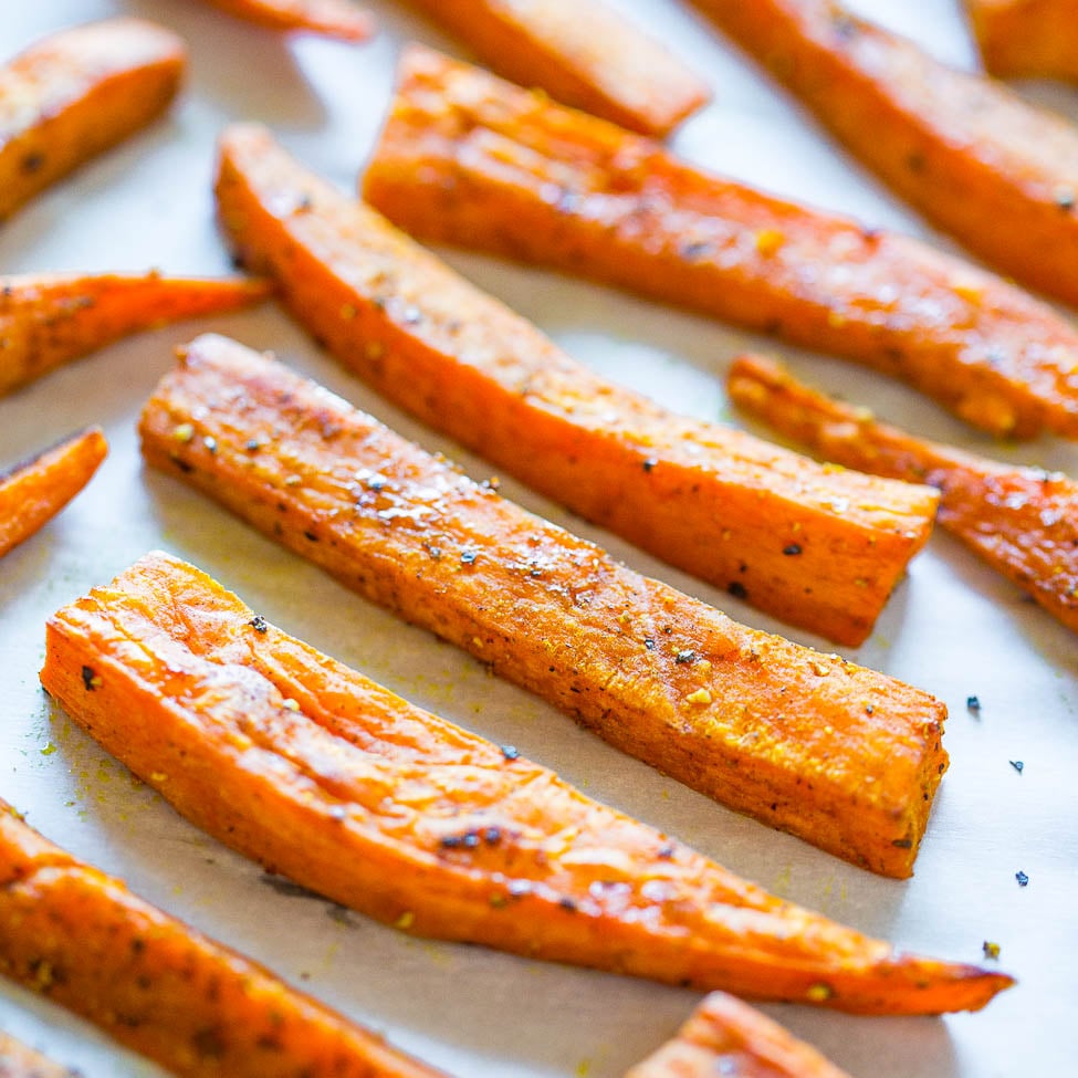 Roasted carrot sticks seasoned with herbs on a baking sheet.