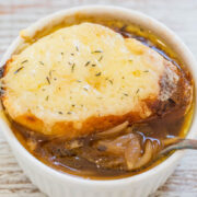A bowl of french onion soup topped with melted cheese and garnished with herbs.