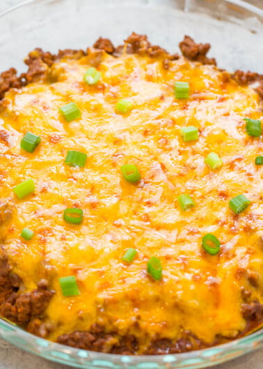 Baked beef casserole topped with melted cheese and chopped green onions in a glass dish.