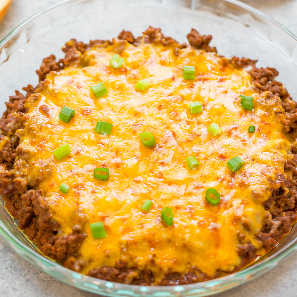 Baked beef casserole topped with melted cheese and chopped green onions in a glass dish.