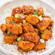 A bowl of sesame chicken served over rice garnished with green onions.