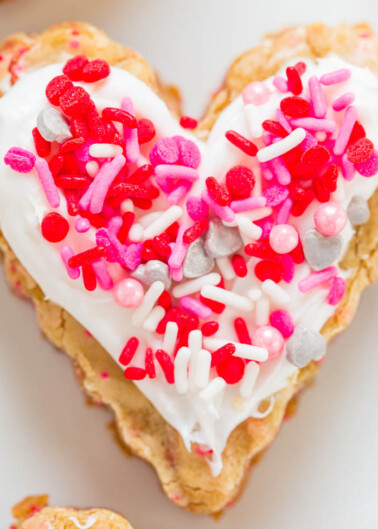 A heart-shaped cookie with white icing and colorful sprinkles.