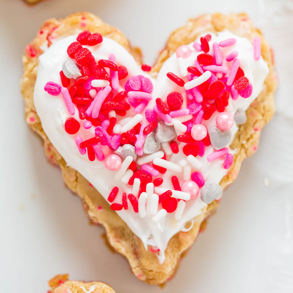 A heart-shaped cookie with white icing and colorful sprinkles.