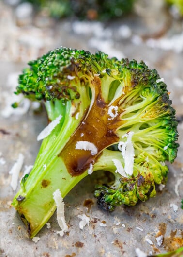 Roasted broccoli floret with melted cheese on a baking sheet.