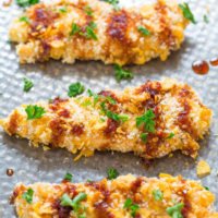 Golden-brown crispy breaded chicken tenders garnished with parsley on a metal surface.
