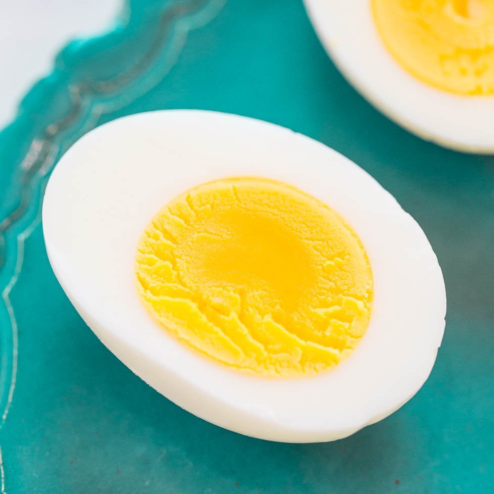 A close-up of a halved boiled egg with a firm yellow yolk on a blue background.