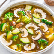 A bowl of vegetable soup with mushrooms, broccoli, and zucchini.
