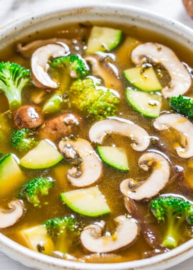 A bowl of vegetable soup with mushrooms, broccoli, and zucchini.