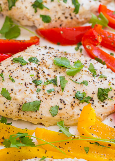 Grilled chicken breasts garnished with parsley alongside sliced red and yellow bell peppers.