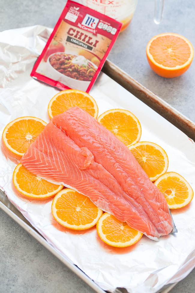 Raw salmon fillet on a bed of orange slices, with a chili mix packet nearby, ready for seasoning or cooking.