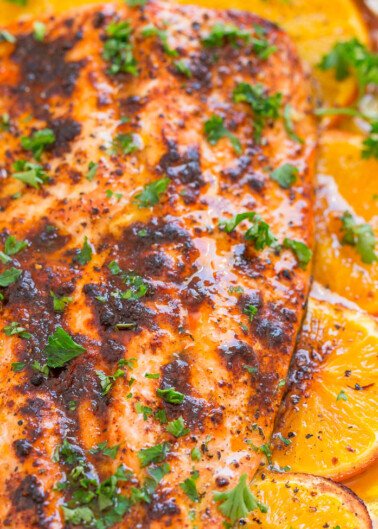 Oven-baked salmon fillet with a glaze, garnished with slices of orange and parsley.