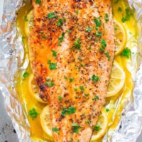 Baked salmon fillet with herbs and lemon slices on aluminum foil.