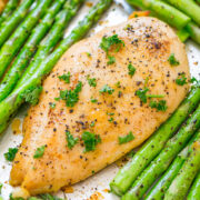Grilled chicken breast garnished with parsley alongside roasted asparagus.