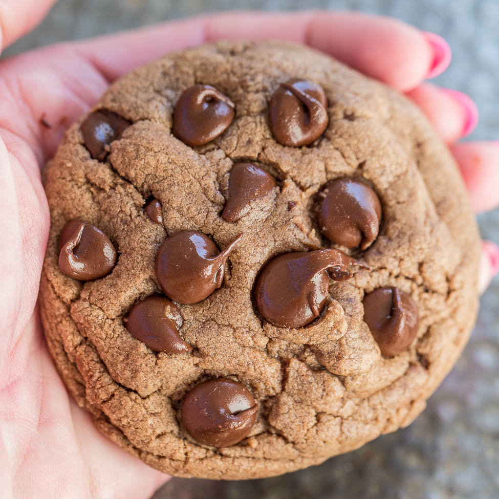 A person holding a freshly baked chocolate chip cookie.