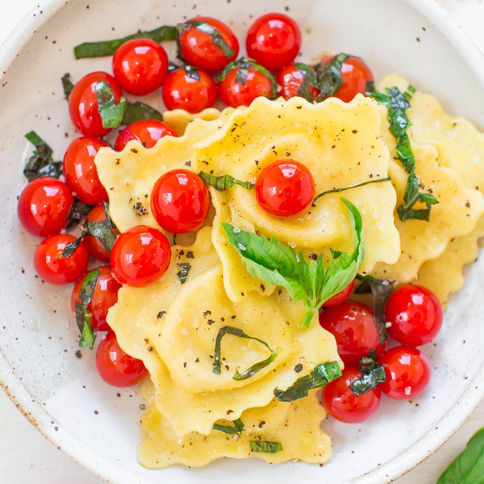 A plate of ravioli garnished with cherry tomatoes and basil leaves.