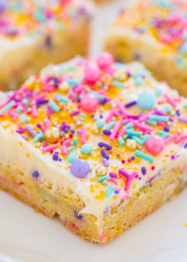 A slice of vanilla frosted cake with colorful sprinkles on a plate.