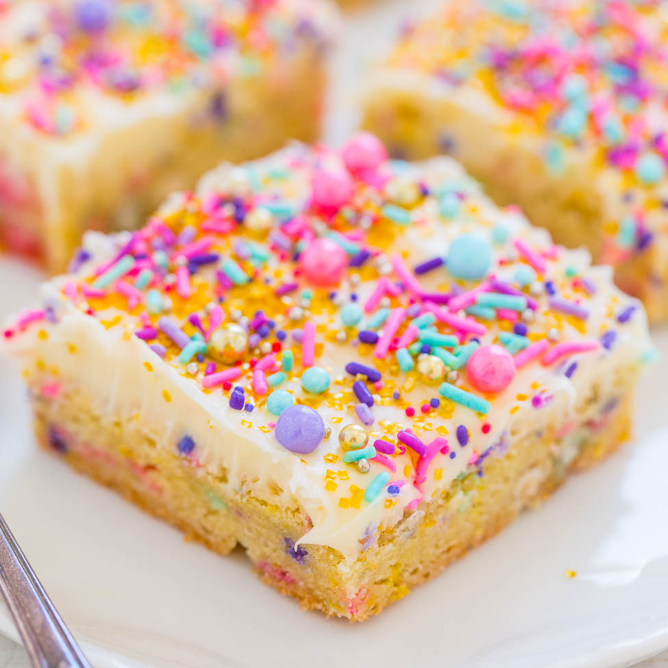 A slice of vanilla frosted cake with colorful sprinkles on a plate.