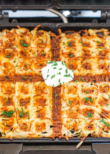 Golden brown hash browns topped with a dollop of sour cream and chives served on an open waffle iron.
