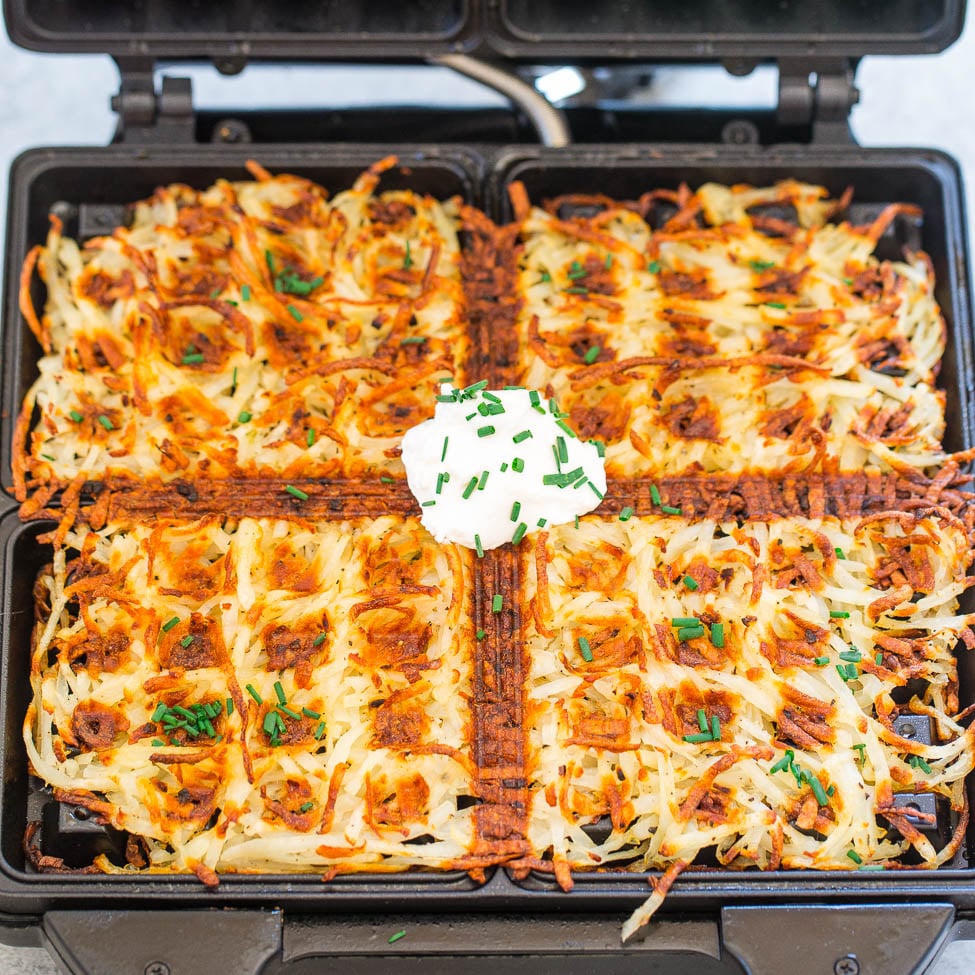Golden brown hash browns topped with a dollop of sour cream and chives served on an open waffle iron.