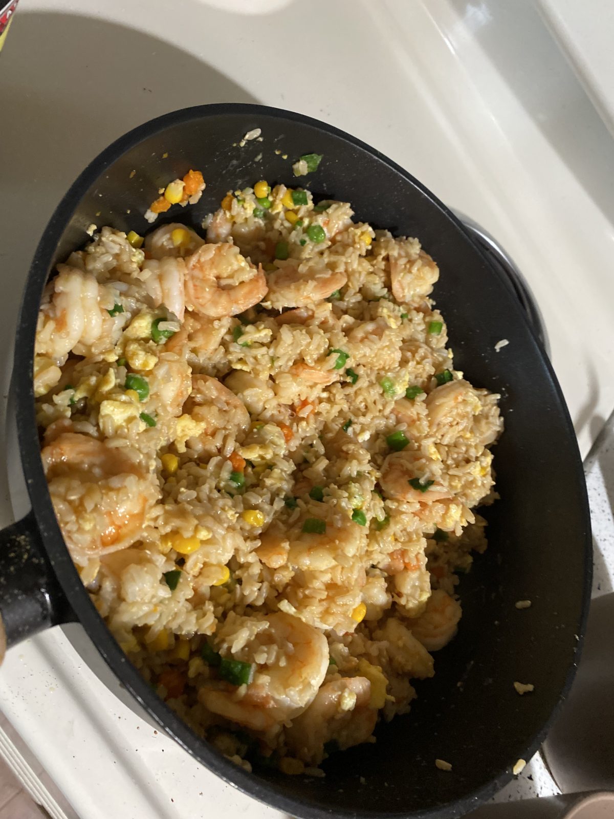 A pan filled with shrimp fried rice containing rice, shrimp, scrambled eggs, peas, corn, and carrots on a kitchen counter.