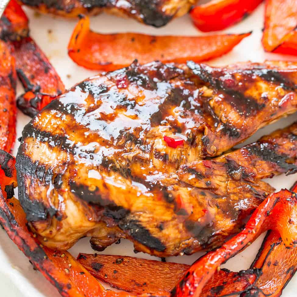Grilled chicken breast with char marks served with roasted red bell peppers.