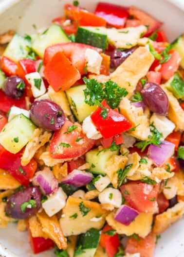 A bowl of mediterranean-style bread salad with tomatoes, cucumbers, onions, olives, and herbs.