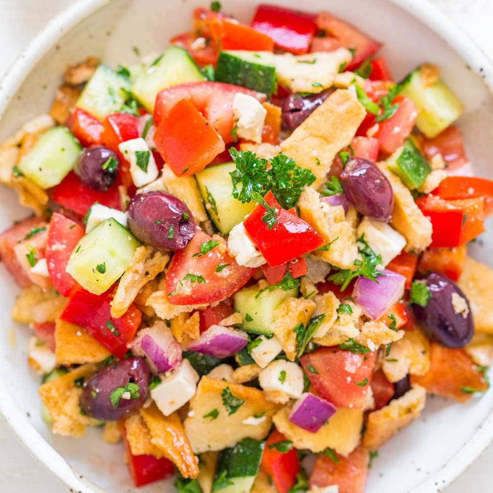 A bowl of mediterranean-style bread salad with tomatoes, cucumbers, onions, olives, and herbs.