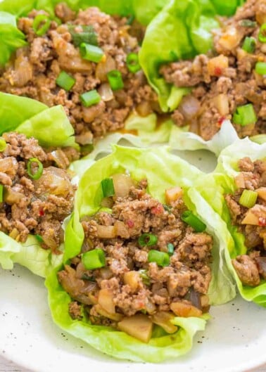 A plate of lettuce wraps filled with savory minced meat and diced vegetables, garnished with sliced green onions.