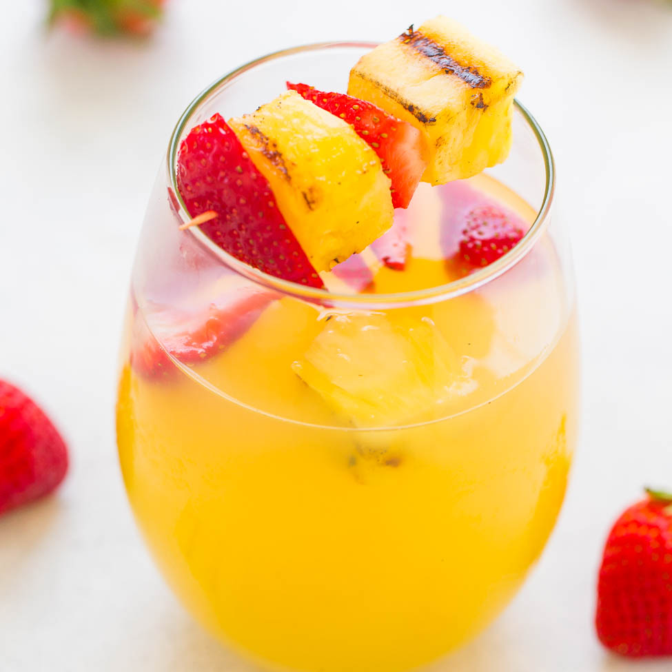 A refreshing tropical drink garnished with skewered strawberries and pineapple.