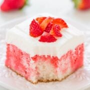 A piece of strawberry-flavored cake with cream topping and fresh strawberry pieces on a decorative plate.