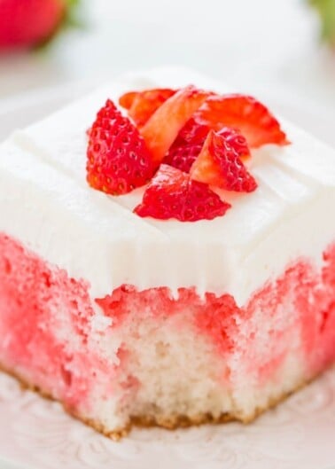 A piece of strawberry-flavored cake with cream topping and fresh strawberry pieces on a decorative plate.