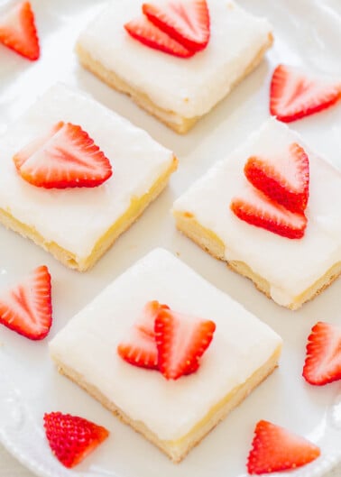 Plate of frosted lemon bars topped with strawberry slices.