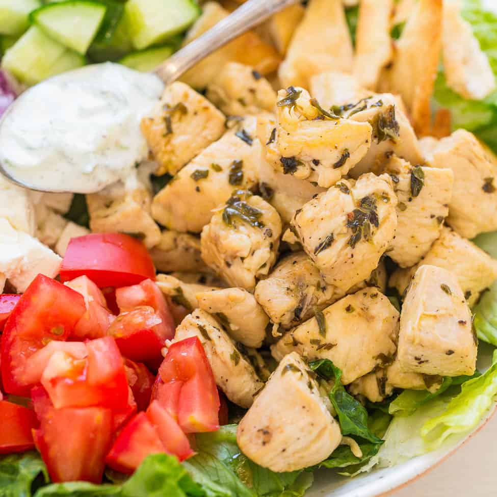 A fresh greek salad with chopped tomatoes, cucumbers, seasoned chicken, and a dollop of tzatziki sauce.