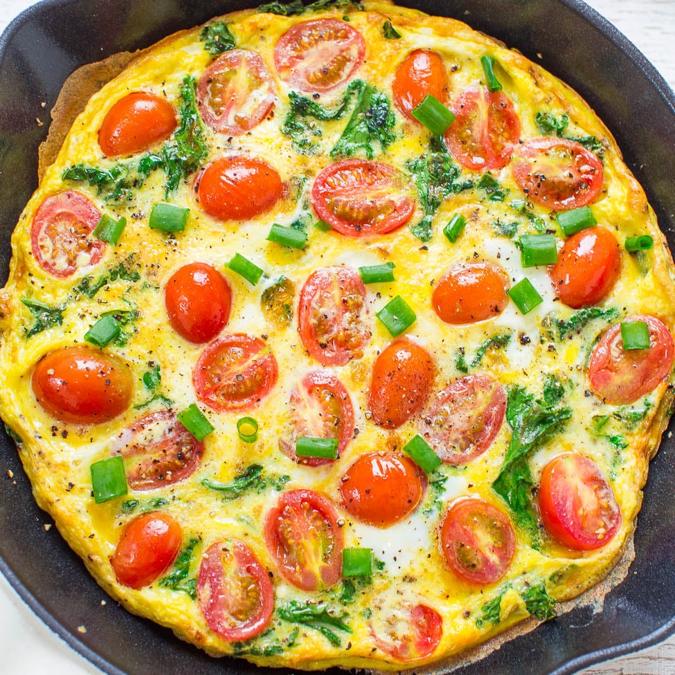 A colorful frittata with halved cherry tomatoes and chopped green onions in a frying pan.