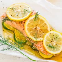 Baked salmon garnished with lemon slices and dill on a bed of zucchini.